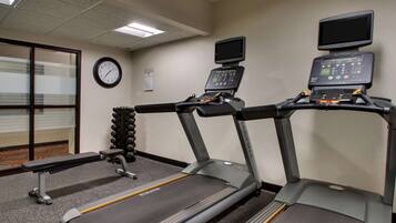 A gym with treadmills, a clock, and a digital screen on the wall.