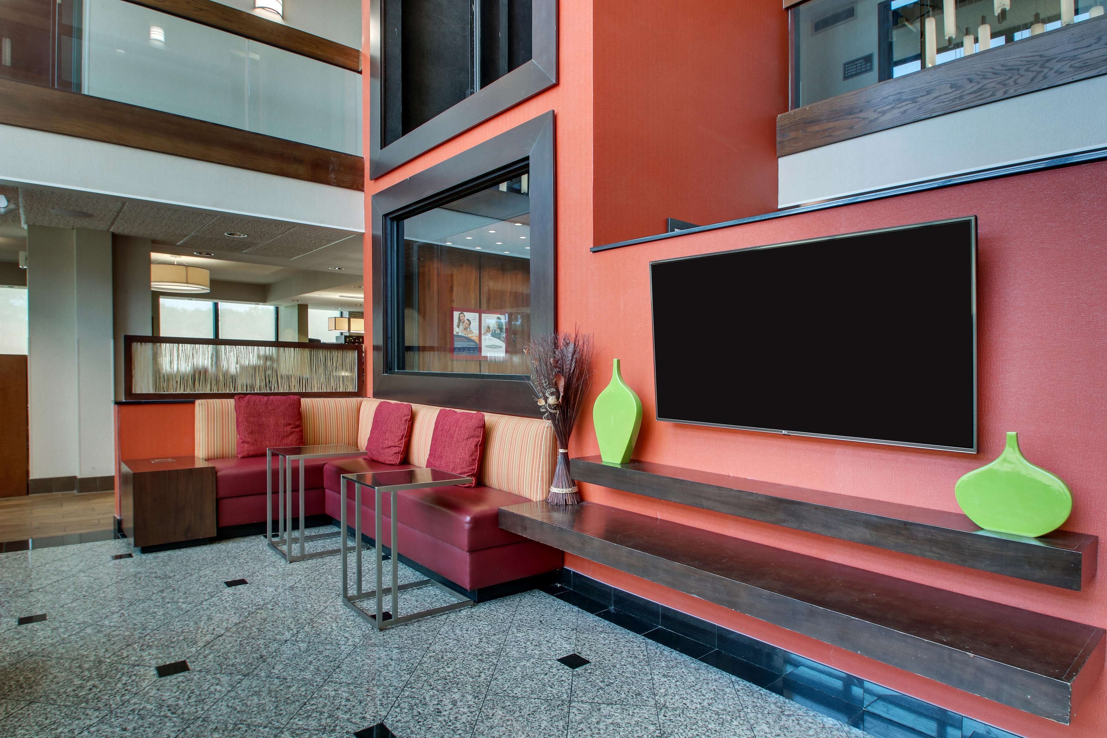 Un lobby moderno con una pared de acento roja, un televisor de pantalla plana grande y una zona de estar con un sofá rojo y una partición de vidrio.