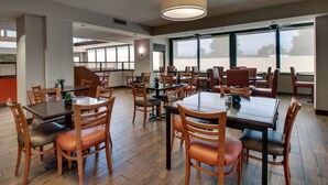 A spacious dining area with multiple tables and chairs, large windows, and a ceiling fan. - Drury Inn & Suites Evansville East (Evansville)
