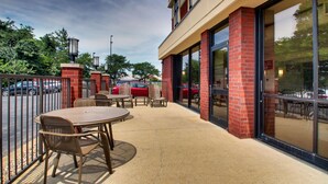 An outdoor patio area with a table and chairs, a brick building with large windows, and a parking lot in the background. - Drury Inn & Suites Evansville East (Evansville)