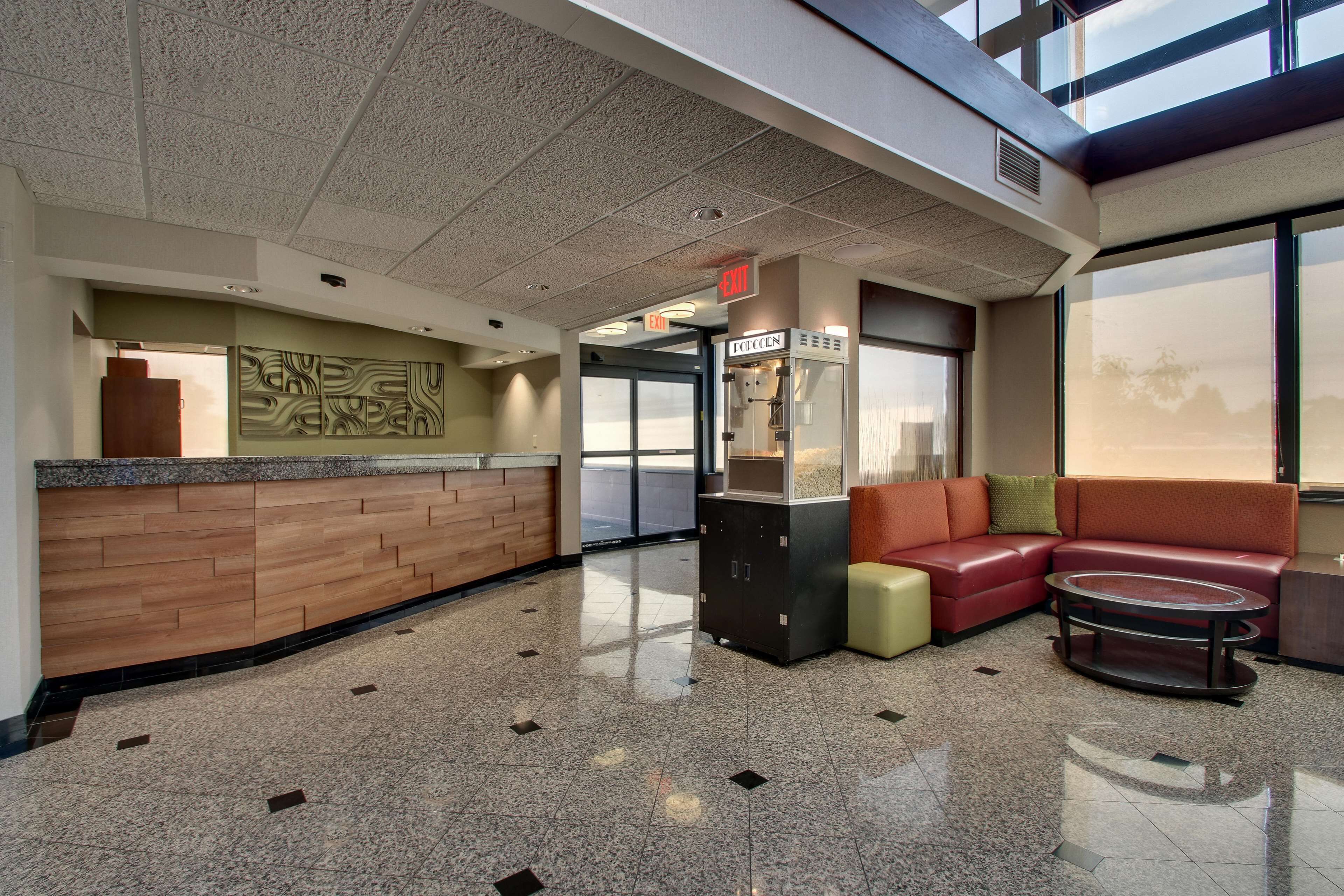 A lobby with a reception desk, a vending machine, a seating area with a sofa and a coffee table, and a glass door leading outside.