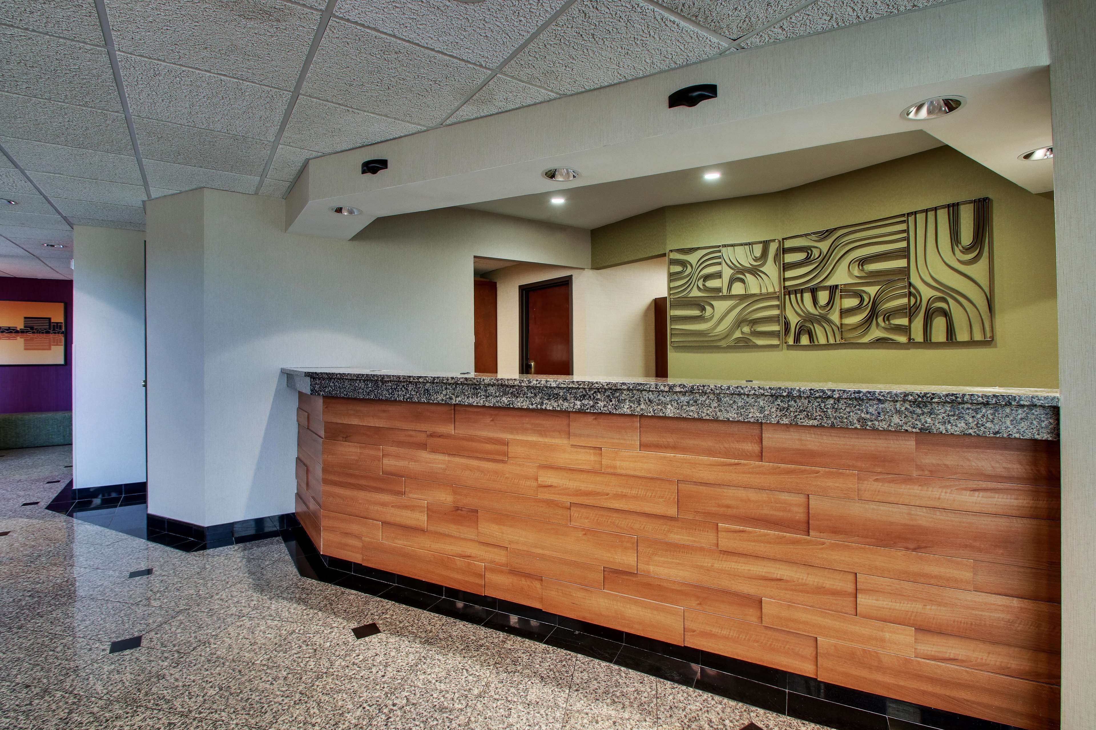 Un área de recepción con un mostrador de madera, una obra de arte abstracta en la pared y suelo de baldosas.