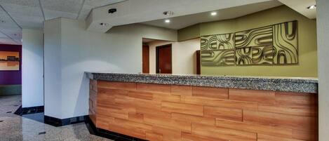 Un área de recepción con un mostrador de madera, una obra de arte abstracta en la pared y suelo de baldosas.