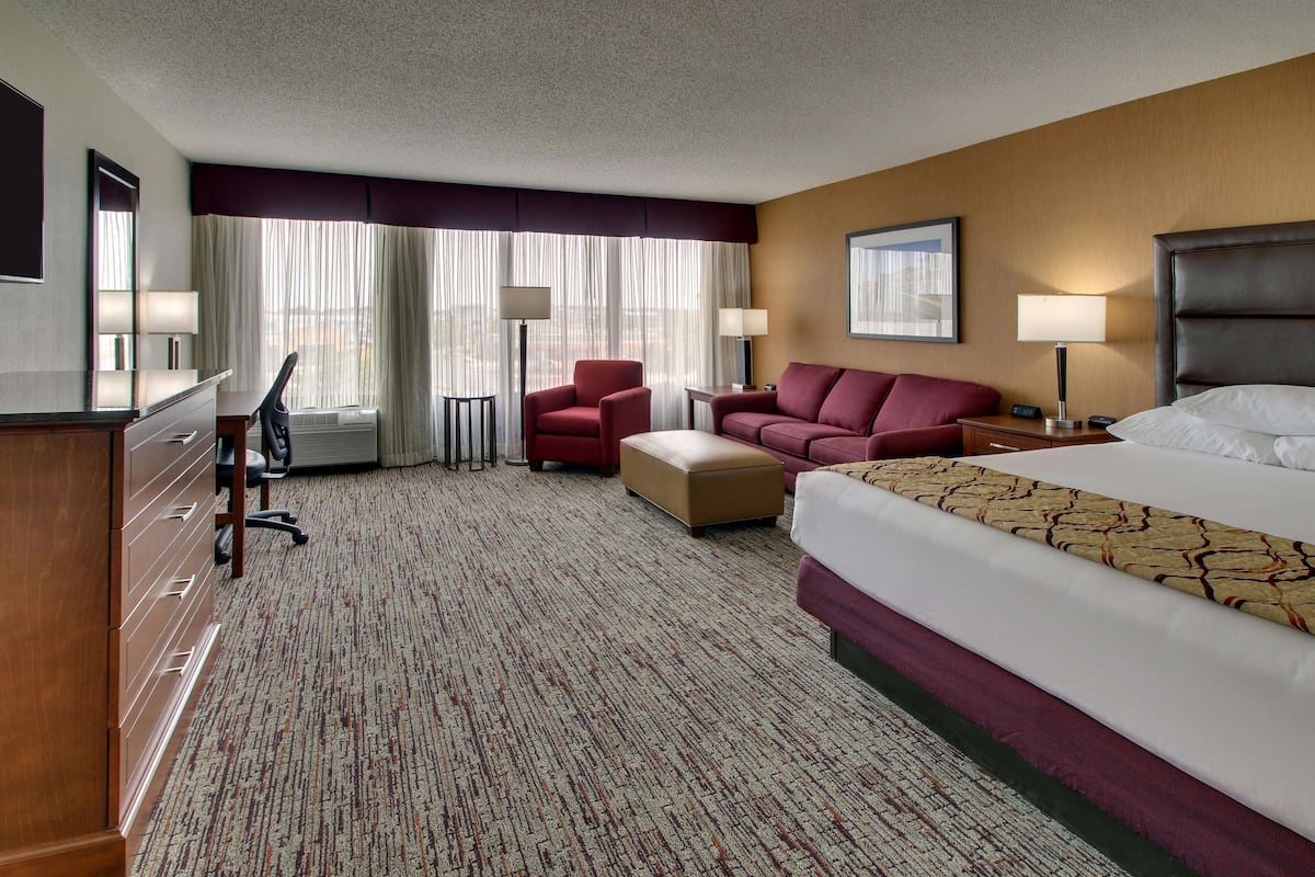 A hotel room with a bed, a desk, a chair, a sofa, and two lamps.