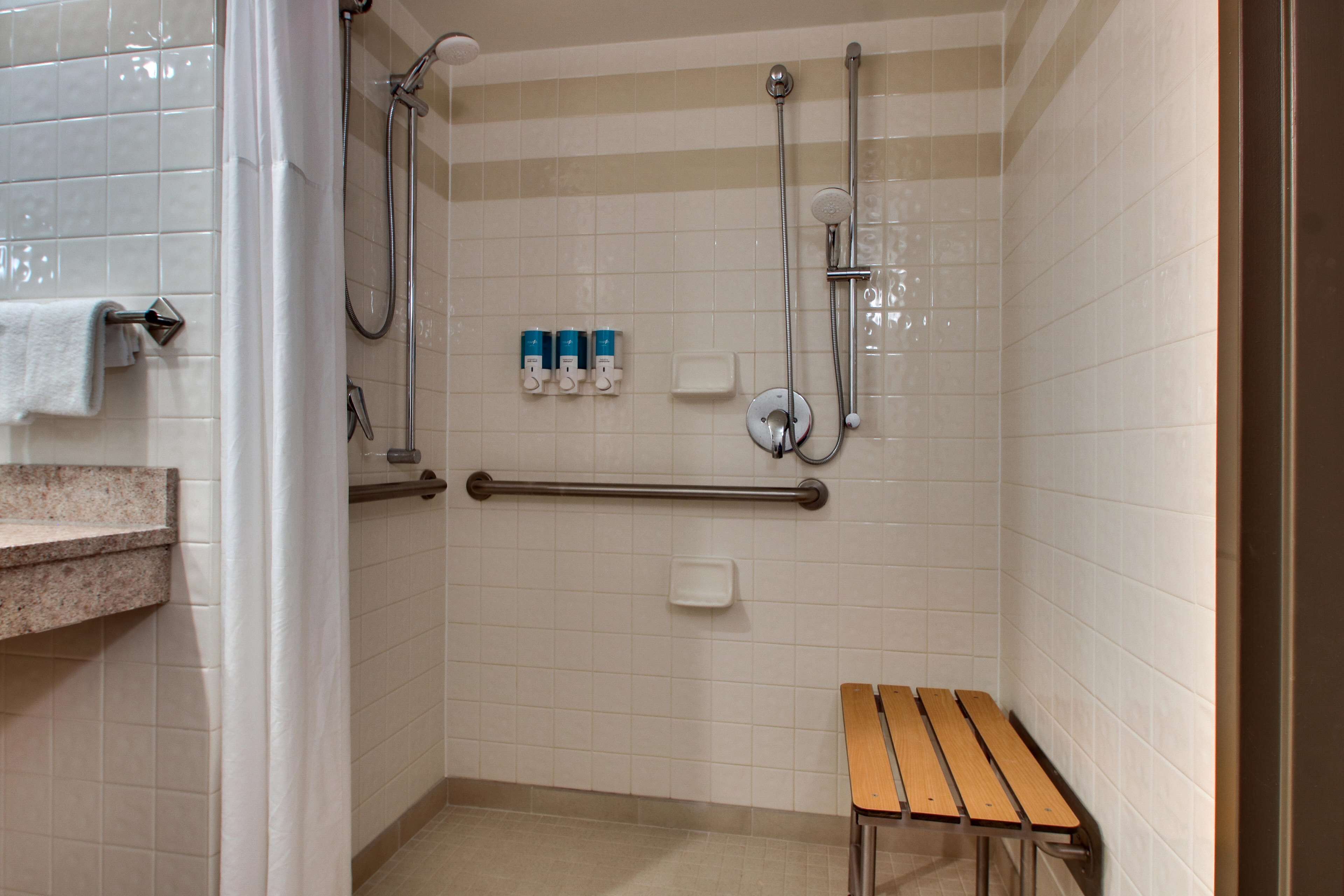 A bathroom with a shower, grab bars, a bench, and a towel rack.