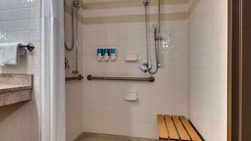 A bathroom with a shower, grab bars, a bench, and a towel rack.