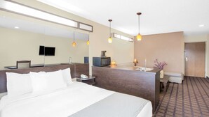 Ein Hotelzimmer mit einem großen Bett, einem Schreibtisch mit Telefon, einer Mikrowelle, einem Fernseher und einem Badezimmer mit Waschbecken und Spiegel.