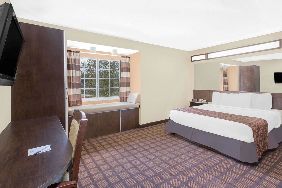 A hotel room with a large bed, a desk, a TV, a window with curtains, and a patterned carpet.