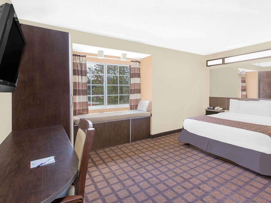 Quarto de hotel com uma cama grande, uma escrivaninha, uma televisão, uma janela com cortinas e um tapete estampado.