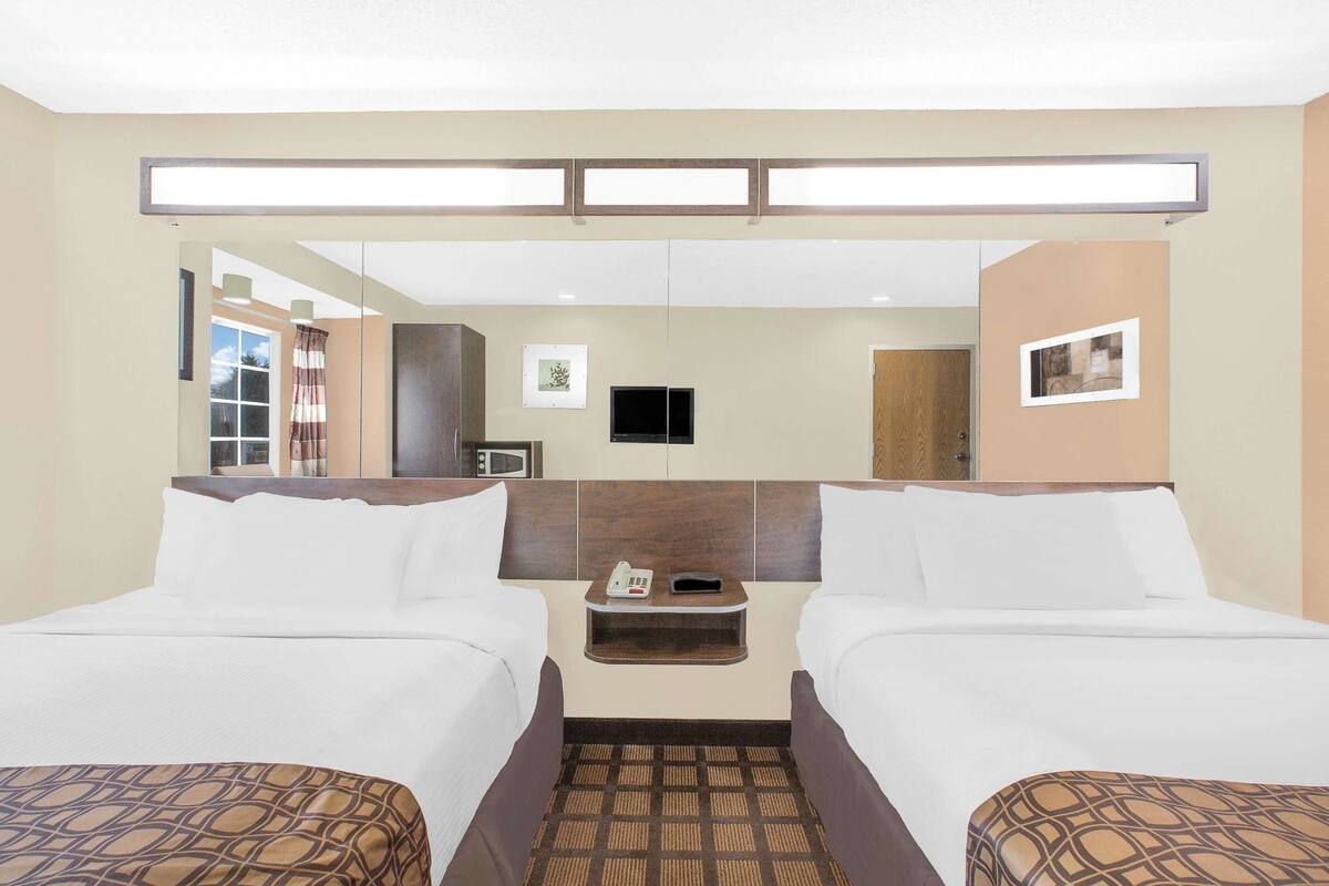 A hotel room with two beds, a flat-screen TV, a microwave, and a small table with a phone and a remote control.
