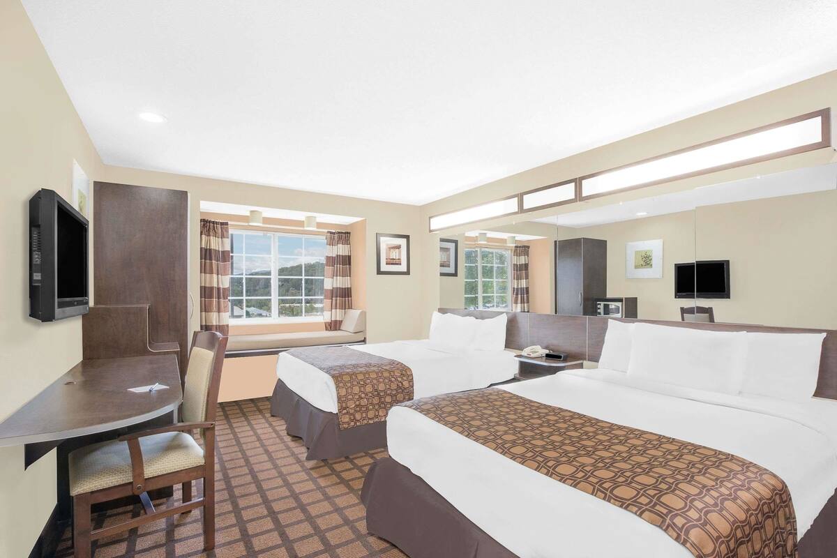A hotel room with two beds, a desk, a chair, a TV, and a window with curtains.
