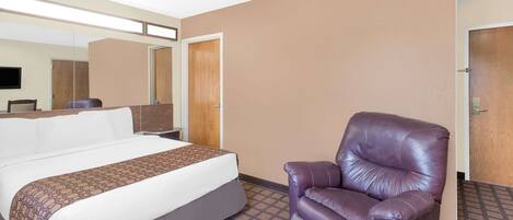 Una habitación de hotel con cama, una silla, un espejo y una puerta.