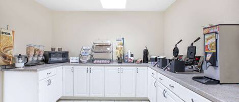 A kitchen with white cabinets, a microwave, a coffee machine, and various appliances.