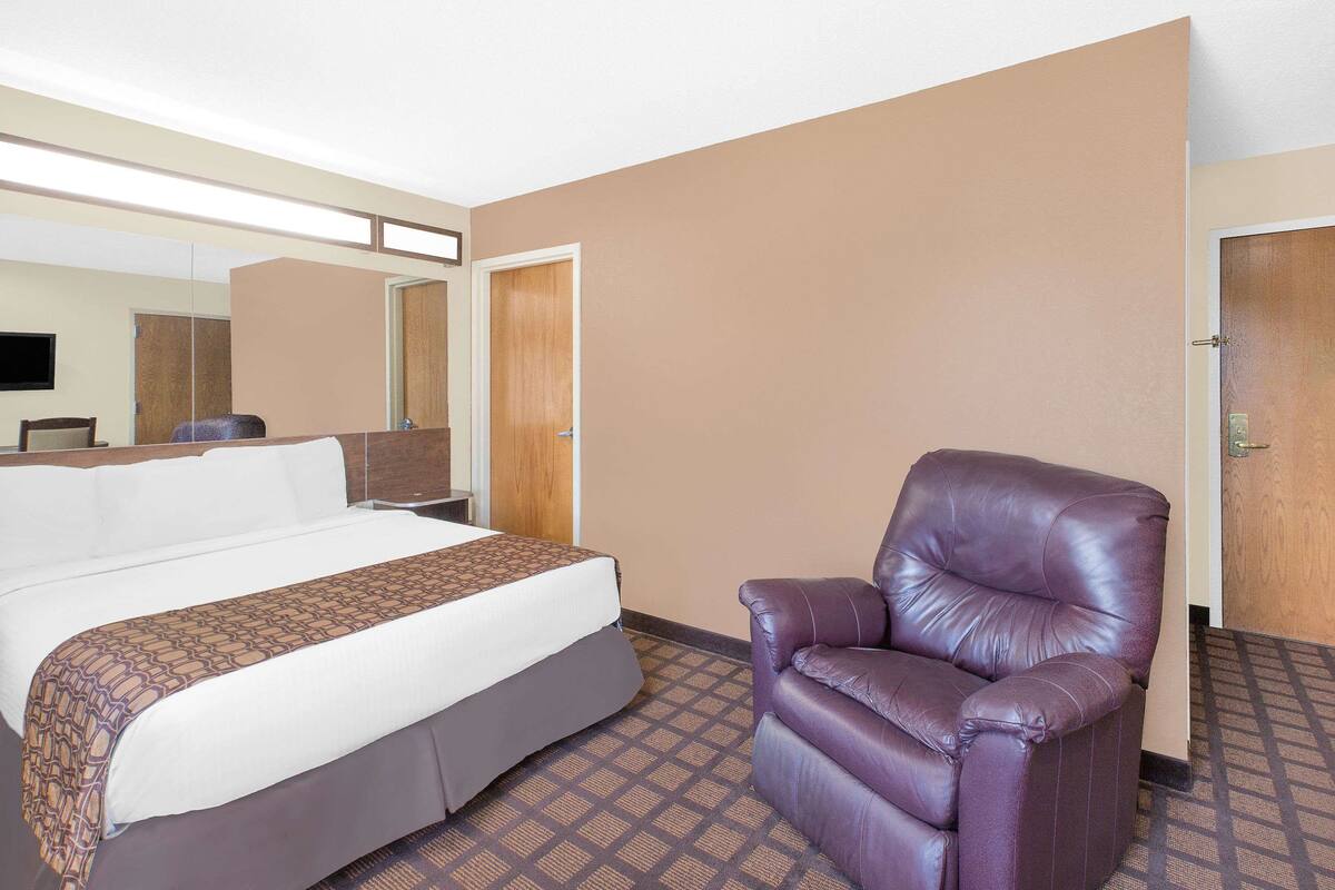 A hotel room with a bed, a leather armchair, a mirror, and a door.