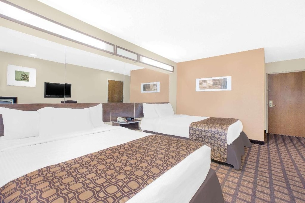 Quarto de hotel com duas camas, televisão de tela plana, mesa de cabeceira e porta.