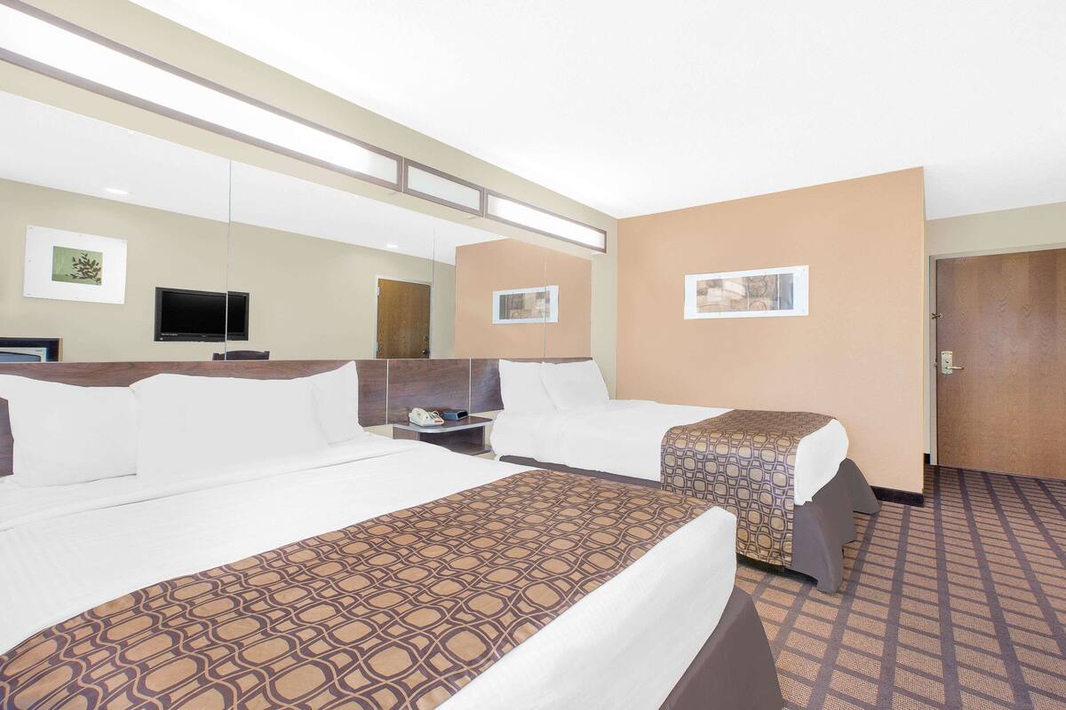 A hotel room with two beds, a TV, a desk, and a door.