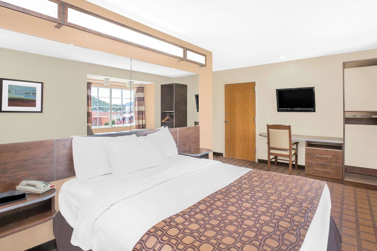 A hotel room with a bed, a desk, a chair, a TV, and a phone on the nightstand.