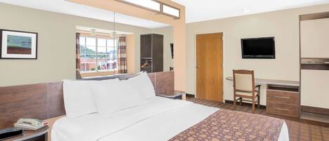 A hotel room with a bed, a desk, a chair, a TV, and a phone on the nightstand.