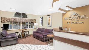 A reception area with a reception desk, a purple sofa, a small round table, and a TV screen. - Microtel Inn by Wyndham Franklin (Franklin)