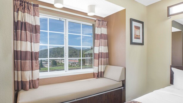 A hotel room with a bed, a window with curtains, a bench, and a framed picture on the wall. - Microtel Inn by Wyndham Franklin (Franklin)