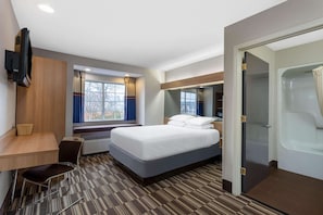 A hotel room with a bed, a desk, a chair, a TV, a window with curtains, and a bathroom with a shower and toilet. - Microtel Inn by Wyndham Matthews/Charlotte (Matthews)