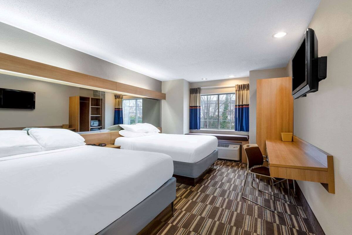 A hotel room with two beds, a desk, a TV, a mirror, and a window with curtains.