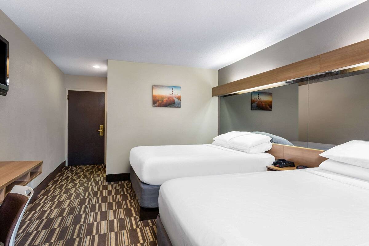 A hotel room with two beds, a desk, a chair, a phone, and a door.