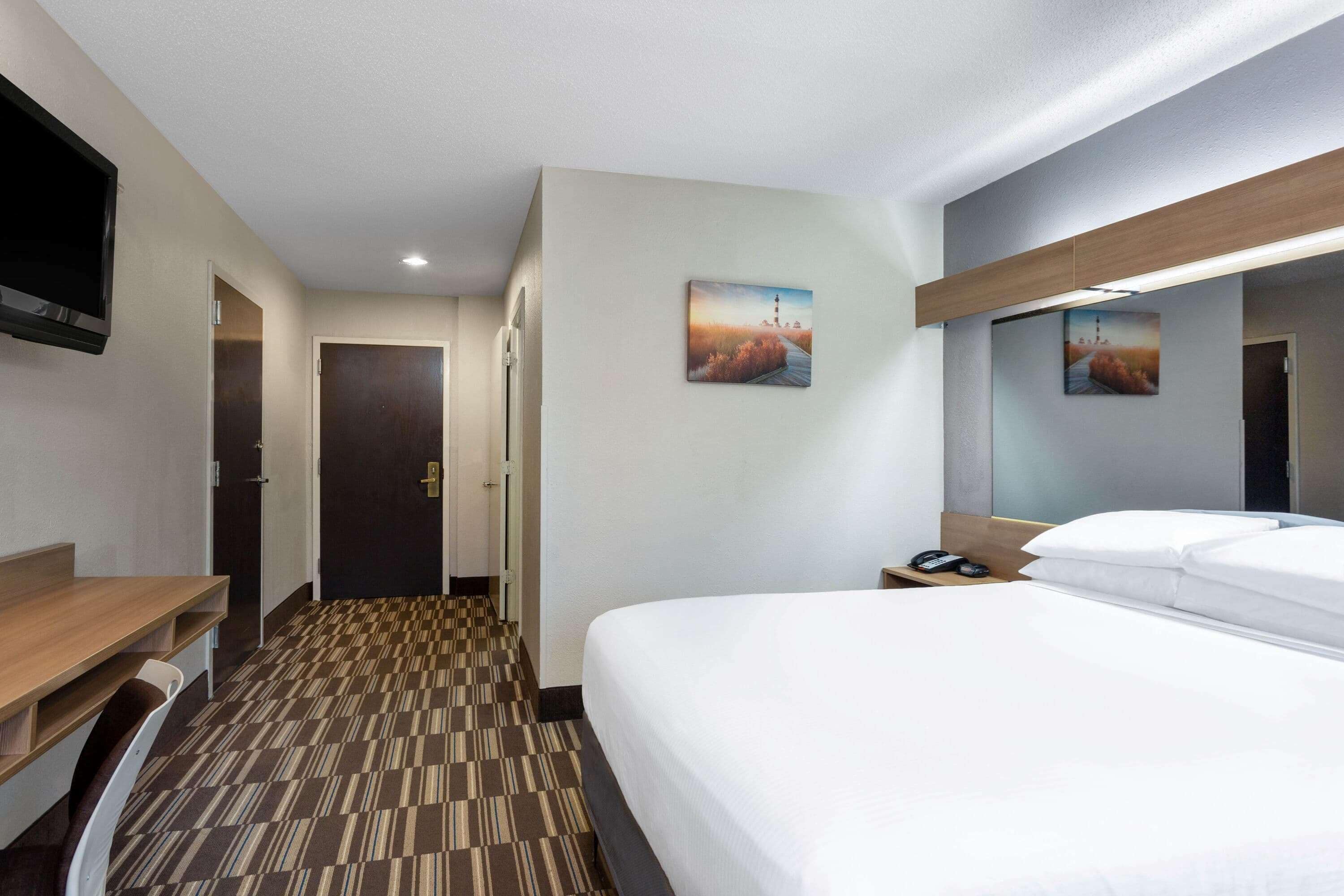 Une chambre d’hôtel avec un lit, un bureau, une chaise, une télévision et deux portes.