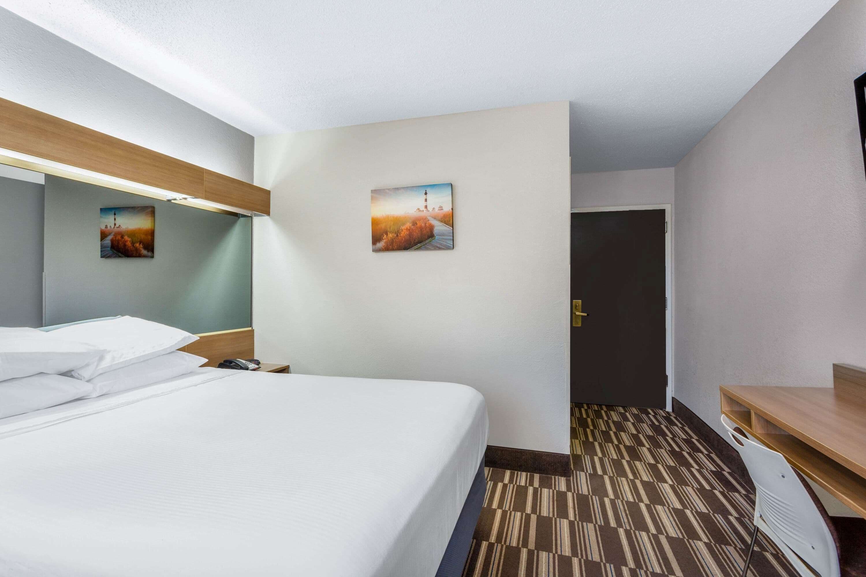 A hotel room with a bed, a desk, and two paintings on the wall.