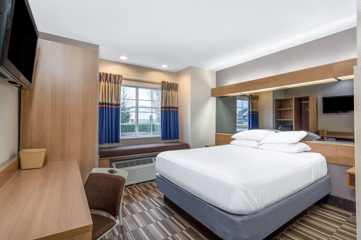 A hotel room with a large bed, a desk, a chair, a TV, and a window with curtains.