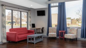 A living room with a red sofa, two patterned chairs, a small table, and a TV mounted on the wall. - Microtel Inn by Wyndham Cornelius/Lake Norman (Cornelius)