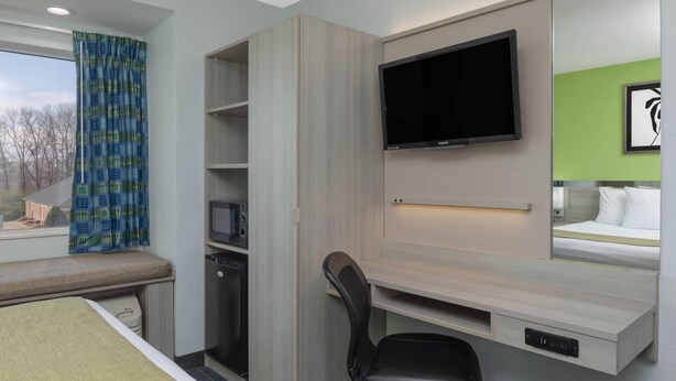A hotel room with a bed, a desk with a chair, a television, a microwave, and a window with curtains. - Microtel Inn by Wyndham Cornelius/Lake Norman (Cornelius)