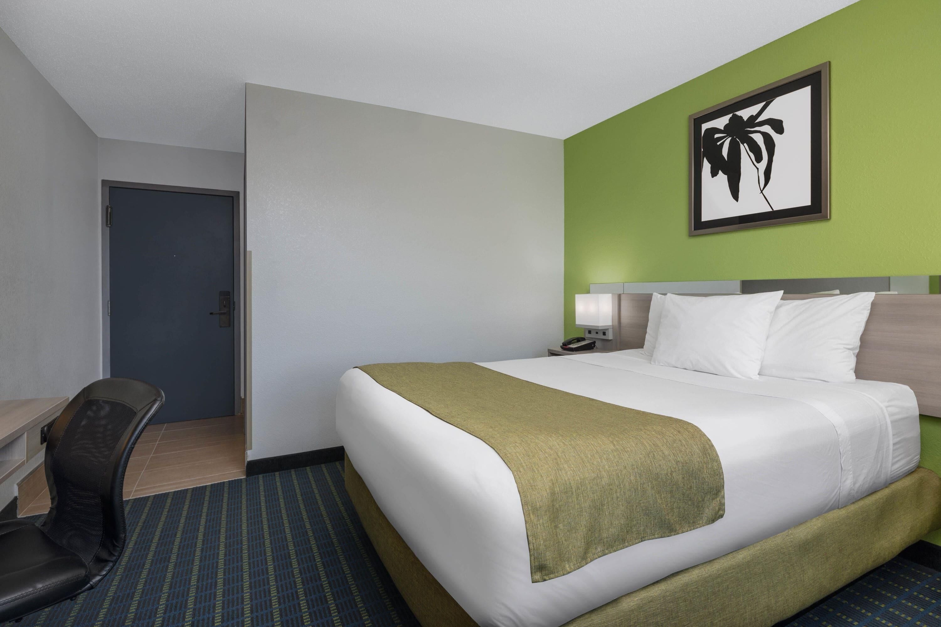 A hotel room with a bed, a desk, a chair, and a framed picture on the wall.
