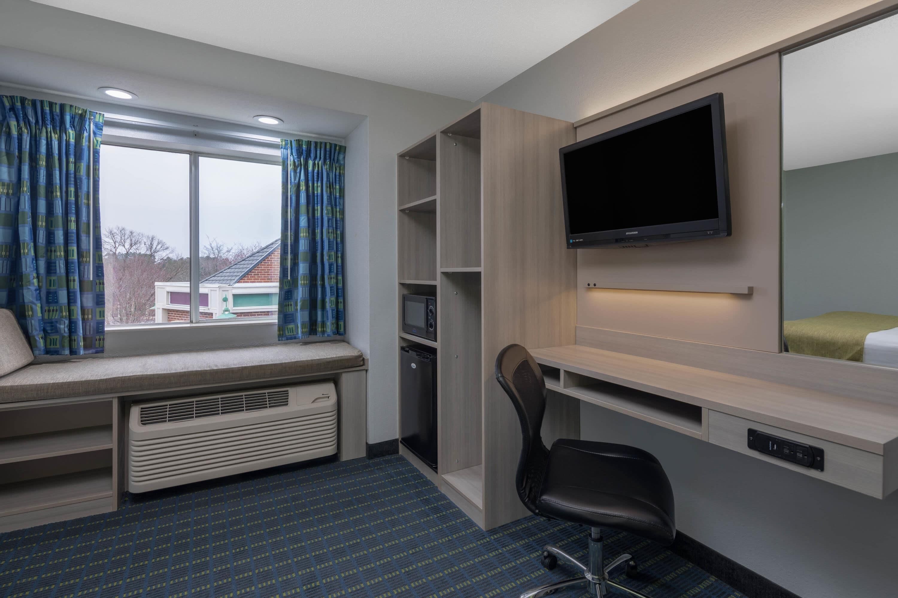 A hotel room with a large window, built-in desk, TV, and seating area.