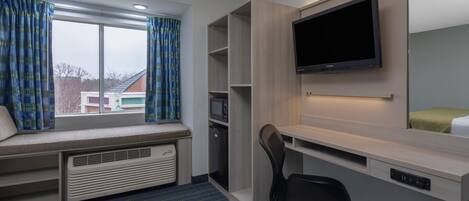 A hotel room with a large window, built-in desk, TV, and seating area.