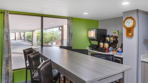 A restaurant with a long table and chairs, a coffee machine, and a clock on the wall. - Microtel Inn by Wyndham Cornelius/Lake Norman (Cornelius)