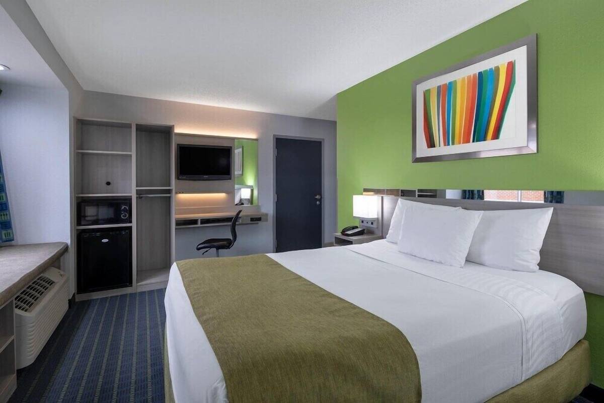 A hotel room with a bed, desk, chair, TV, and a painting on the wall.