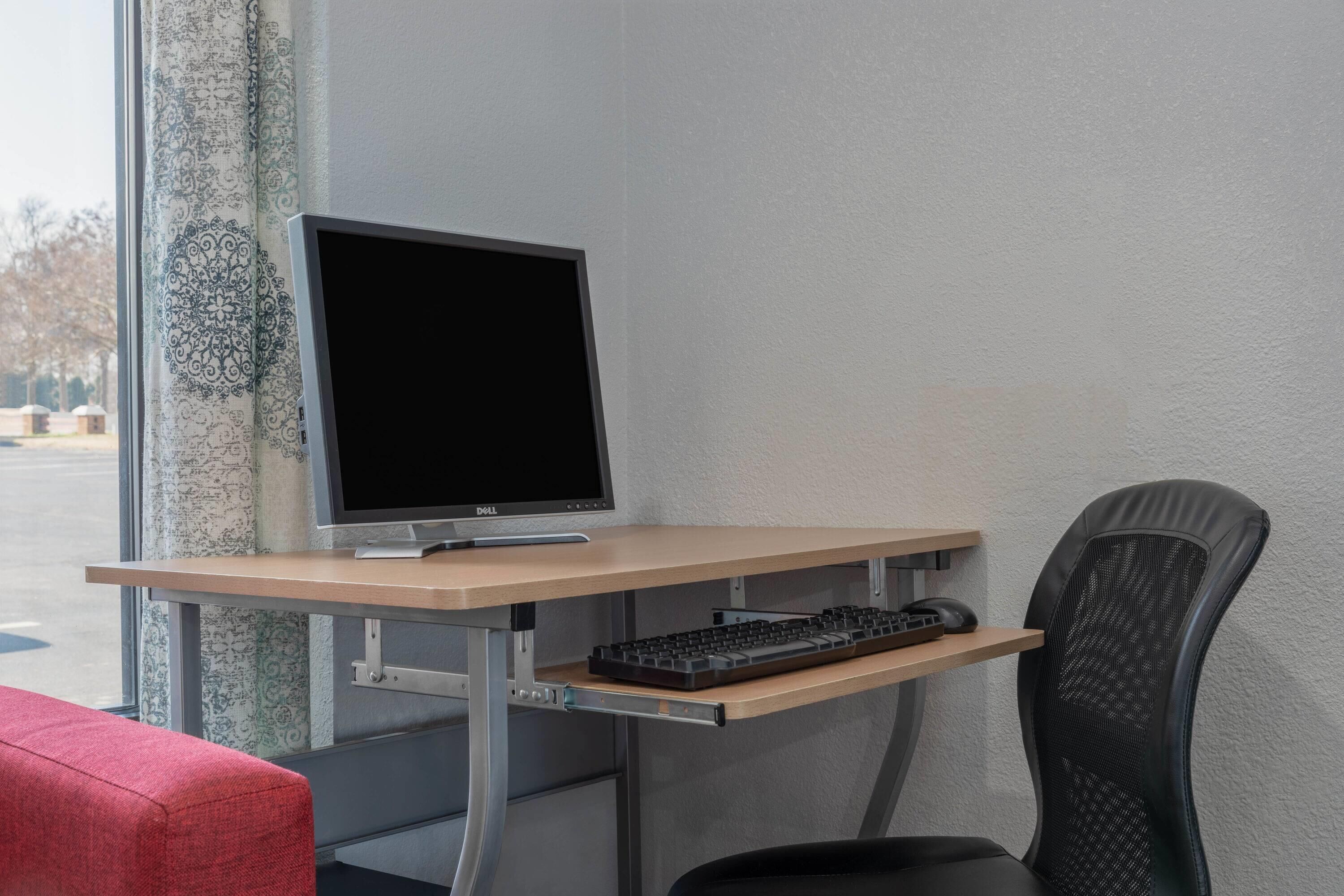 A computer desk with a monitor, keyboard, and chair.
