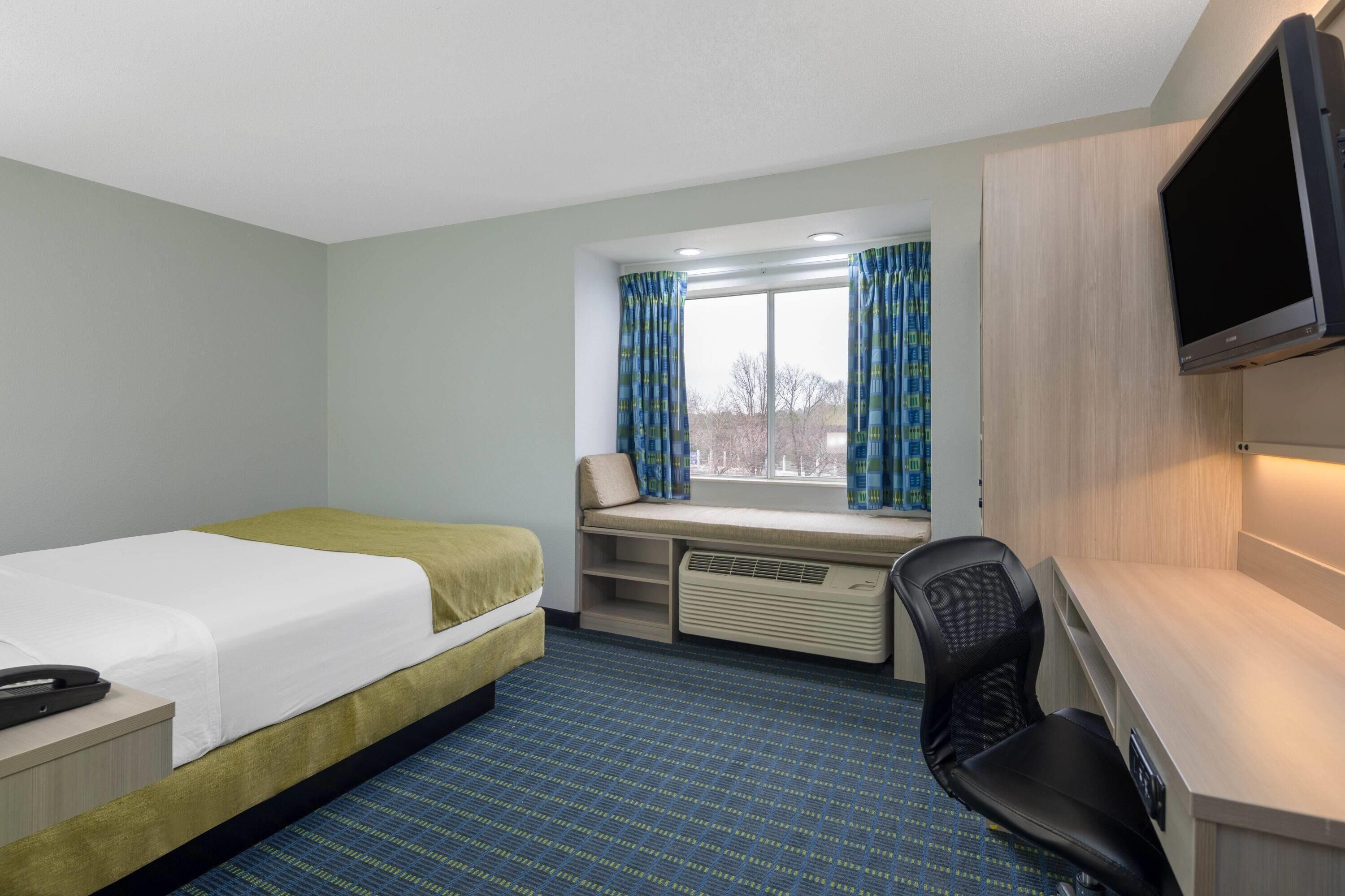 A hotel room with a bed, a desk, a chair, a TV, and a window with curtains.