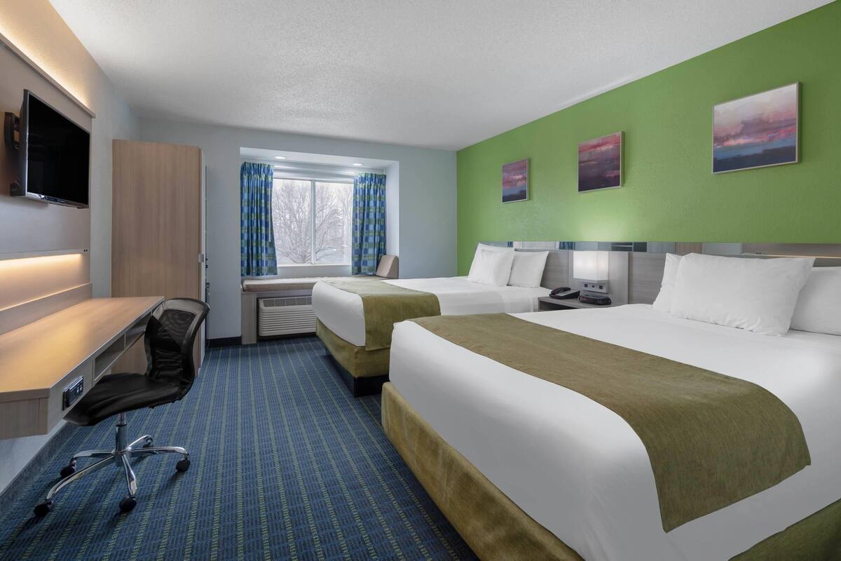 A hotel room with two beds, a desk with a chair, a TV, and a window with curtains.