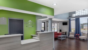 A reception area with a green wall, a reception desk, a red sofa, and patterned chairs. - Microtel Inn by Wyndham Cornelius/Lake Norman (Cornelius)