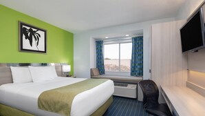 A hotel room with a bed, a desk, a chair, a TV, and a window with curtains. - Microtel Inn by Wyndham Cornelius/Lake Norman (Cornelius)