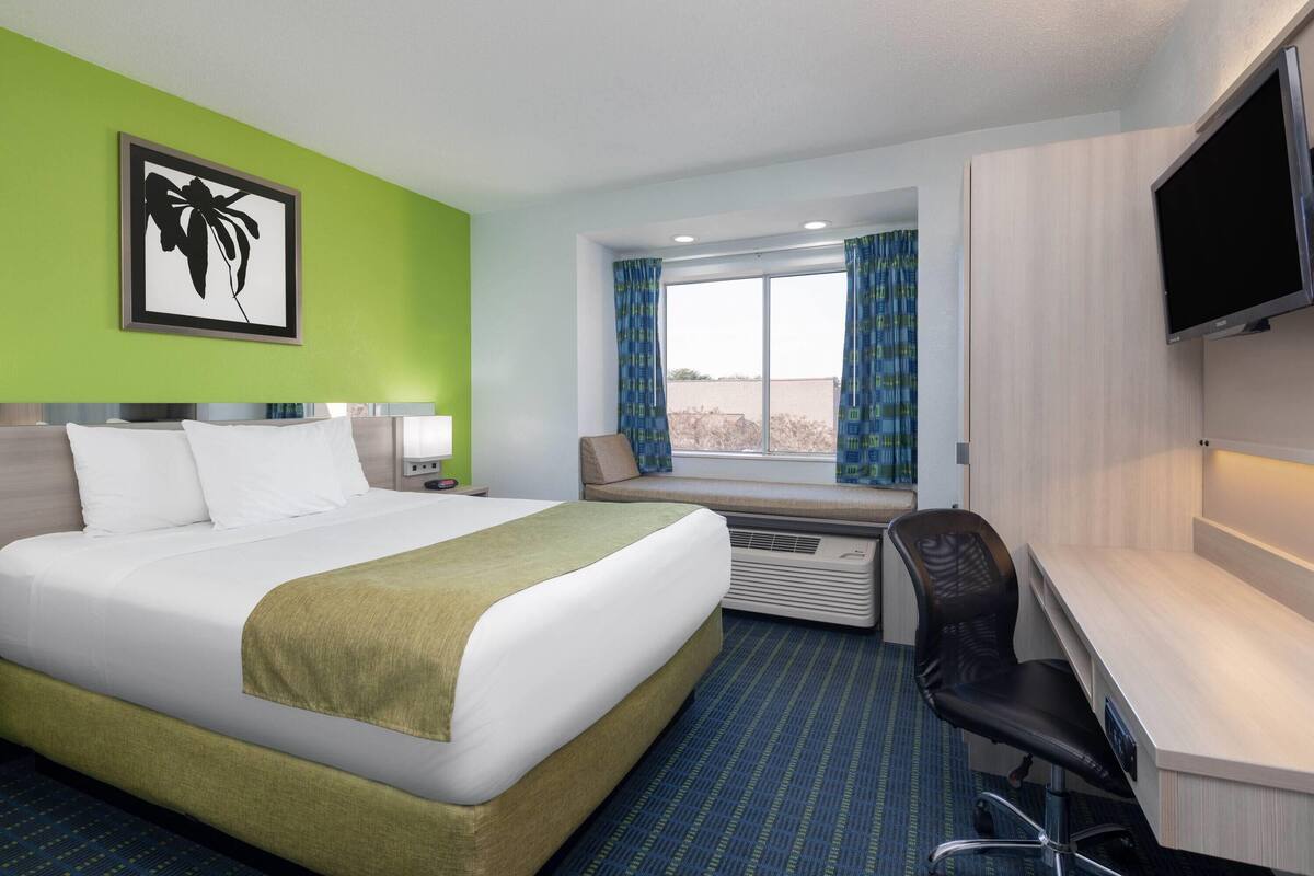 A hotel room with a bed, a desk, a chair, a TV, and a window with curtains.