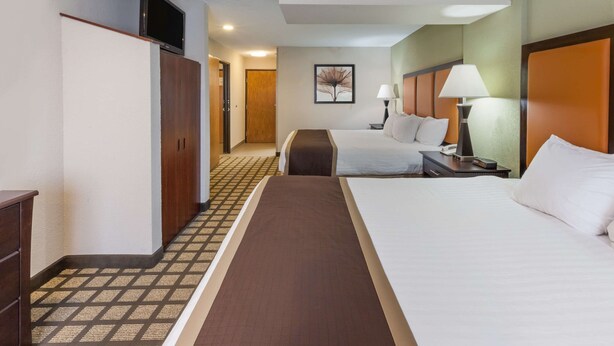 A hotel room with two beds, a television on the wall, and a hallway leading to another room.