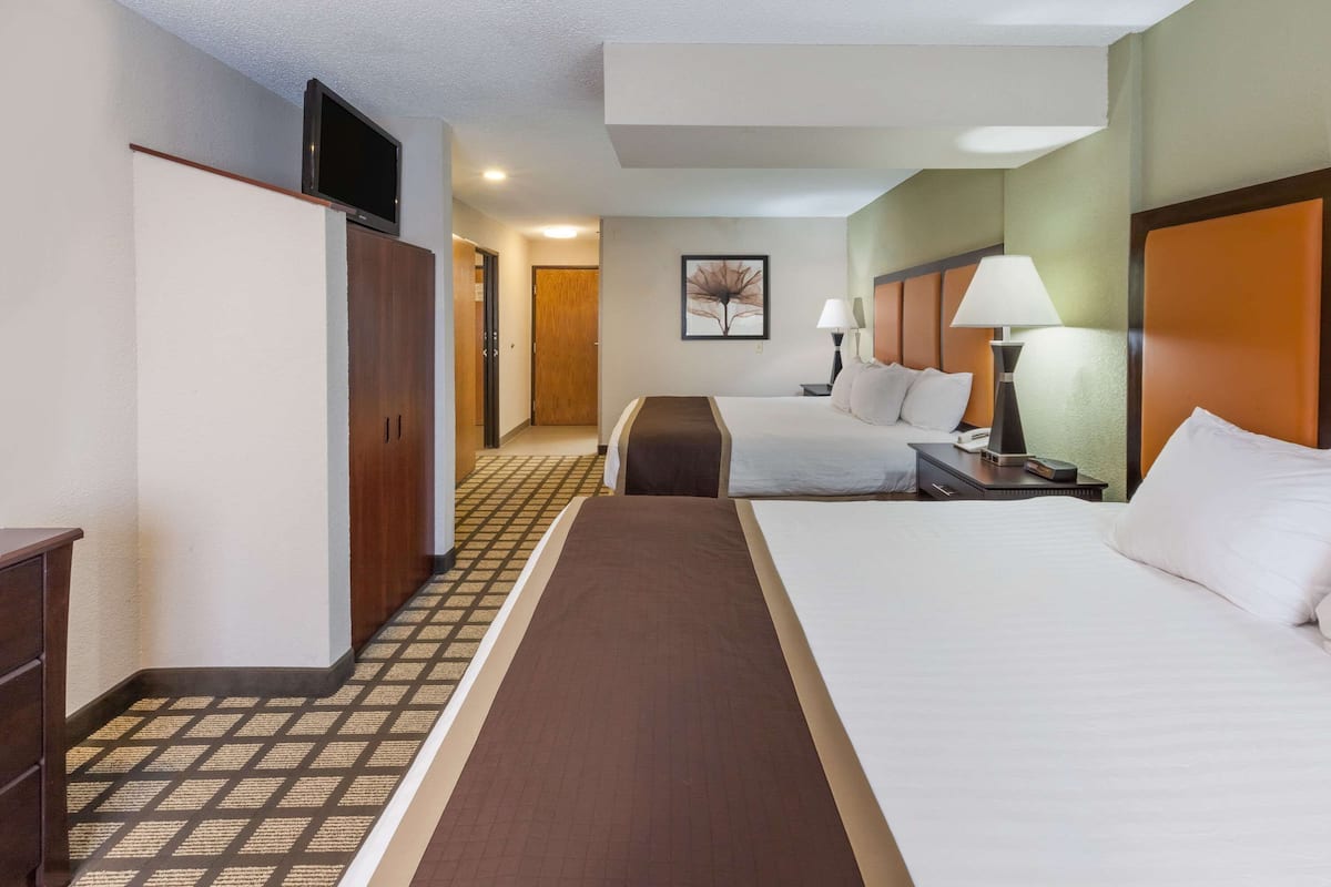 A hotel room with two beds, a television on the wall, and a hallway leading to another room.