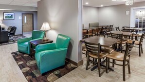 A hotel room with a dining area featuring multiple tables and chairs, a green sofa, and a lamp.