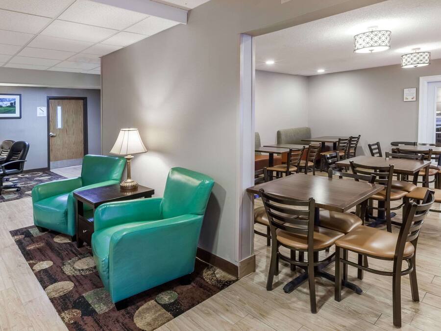 A hotel room with a dining area featuring multiple tables and chairs, a green sofa, and a lamp.