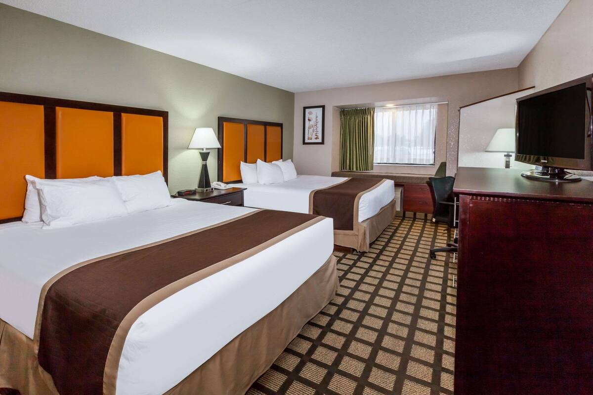 A hotel room with two beds, a desk, a chair, and a television.