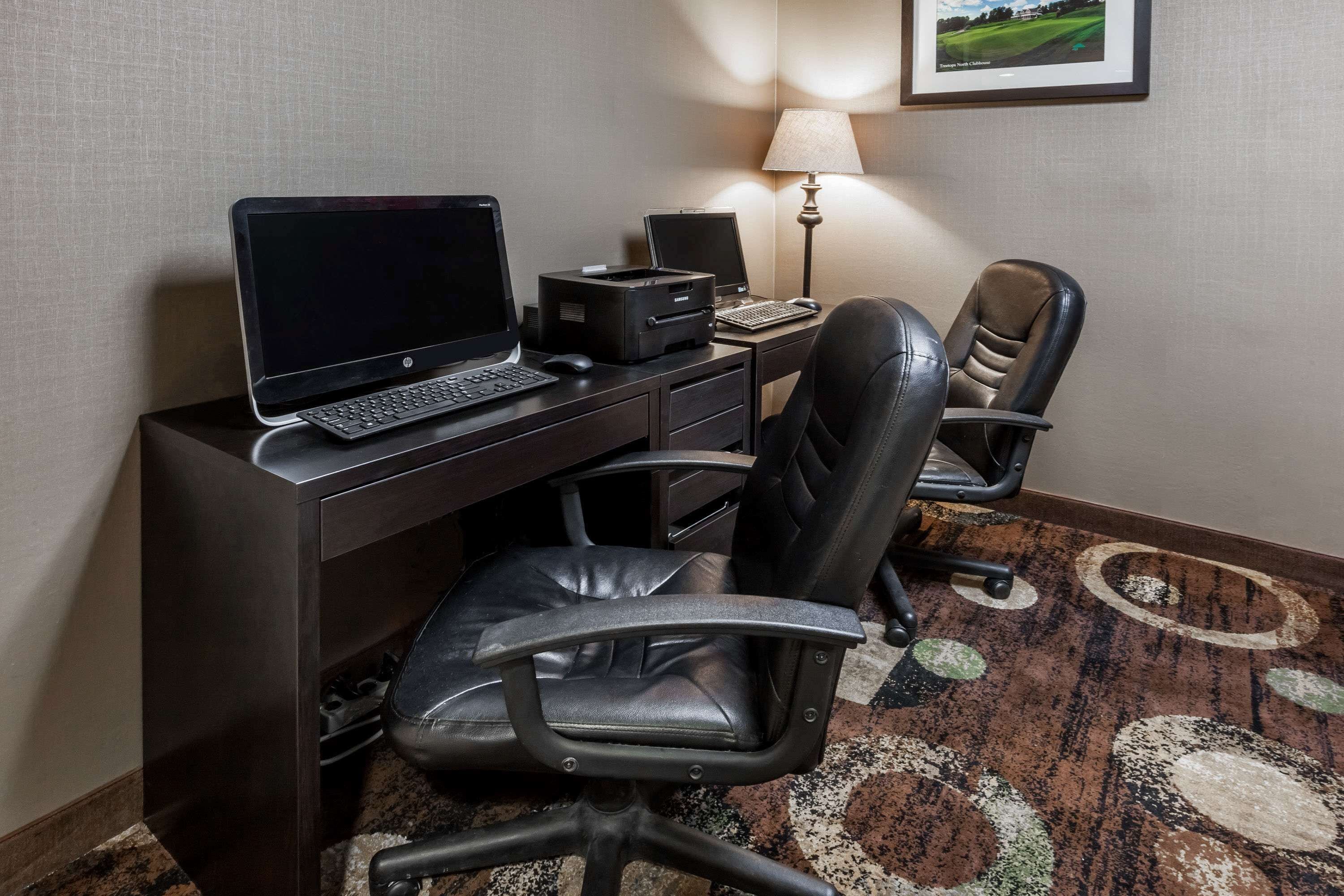 A hotel room with a desk, laptop, printer, and two leather chairs.