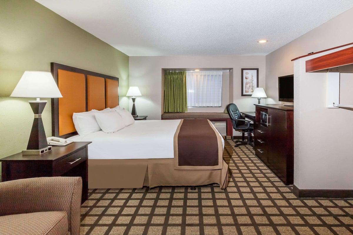 A hotel room with a bed, desk, chair, and a television.